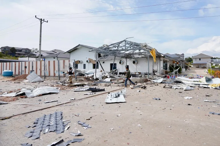 A photo taken and released by Agence Kampuchea Press (AKP) on December 12, 2025 shows men looking at a damaged house following clashes along the Cambodia-Thailand border in Cambodia's Pursat province [AKP/AFP]