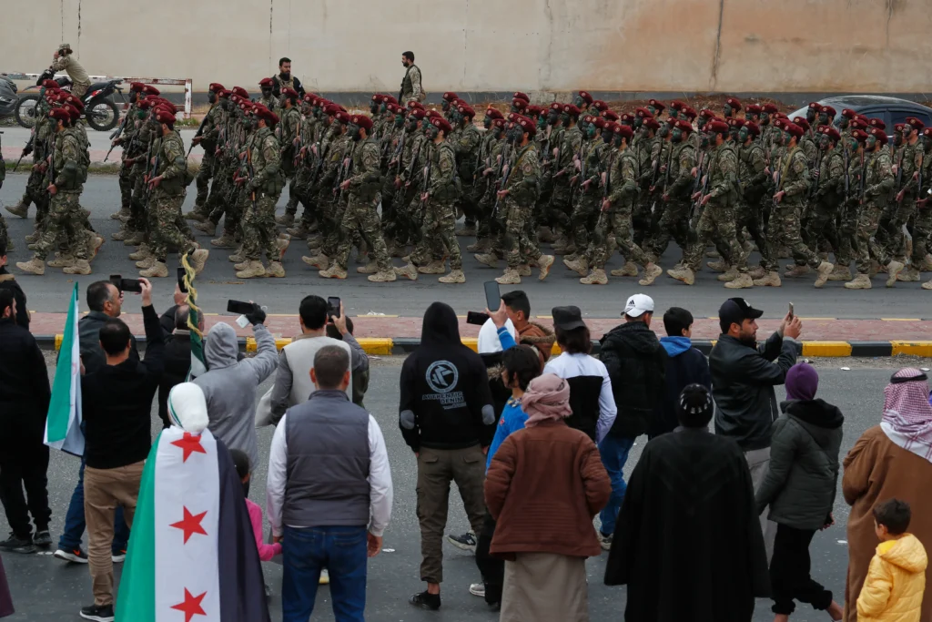 People watch the Syrian army march during a military parade marking the anniversary. [Omar Sanadiki/AP Photo]